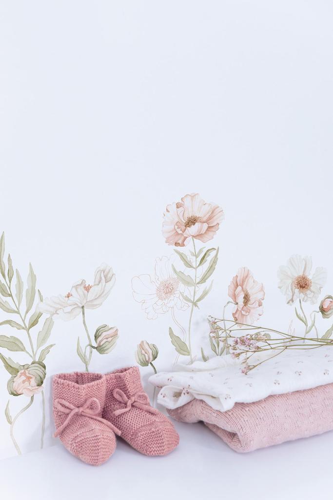 Muursticker met organische zachte roze en beige klaprozen en groene bladeren boven opgevouwen roze en witte babykleding met. - Muursticker | Poppy L/XL - Large - Islandic poppies, kinderkamer, klaproos, lilipinso, Muursticker, vliesbehang - Casa Mini